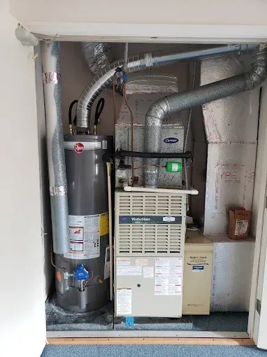 Water heater and furnace installed in a closet. Ductwork and silver insulation are visible.