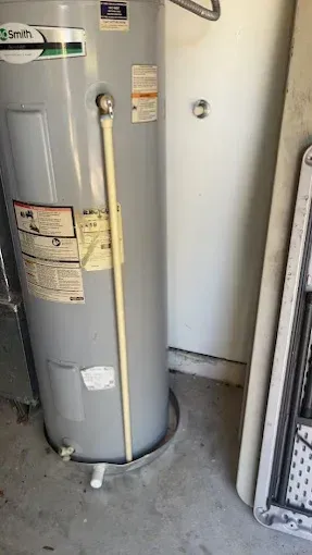 A tall, cylindrical water heater in a garage setting with a white pipe running vertically.