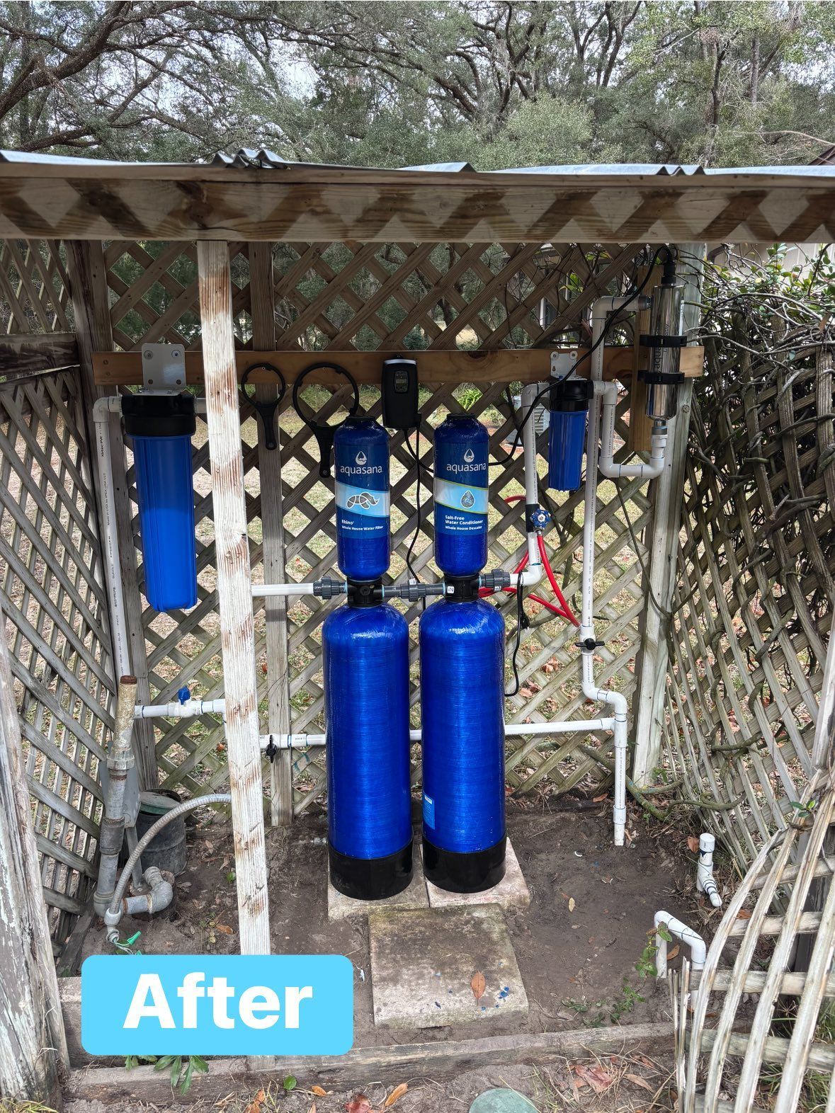 Water filtration system in a white latticed enclosure with blue tanks and pipes.