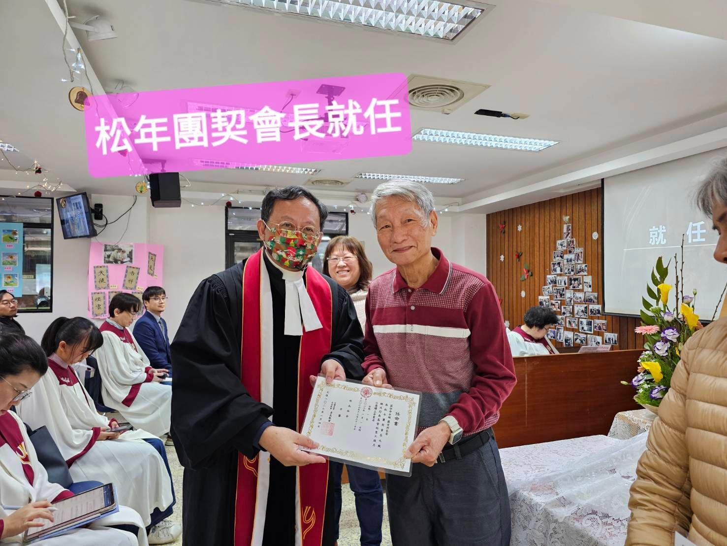 在为资深团契主席举行的仪式上，一名身穿圣袍的人向某人颁发证书。