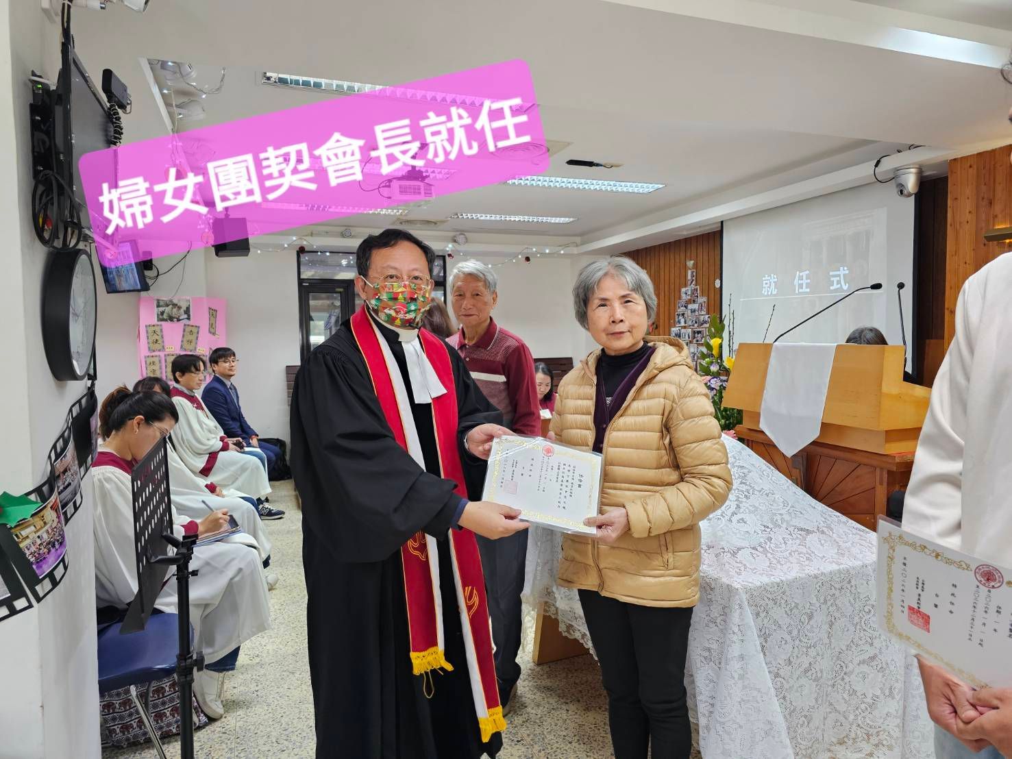 一位身穿长袍的神职人员在教堂仪式上向某人颁发证书，出席者众多。