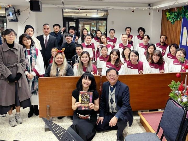 一群人在教堂里，有些人穿着唱诗班长袍，站在一位拿着书的女人和一位跪着的男人身后。