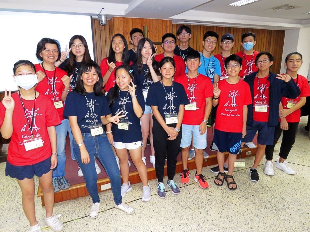 一群身穿配套的红色和藏蓝色活动T恤的人站在一间镶有木板的室内房间里。