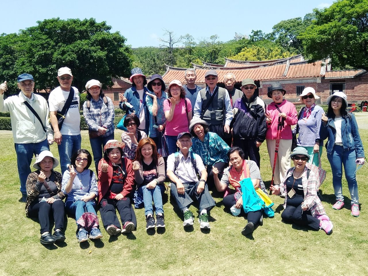 一大群人面带微笑，在传统建筑前的草坪上摆姿势拍照。