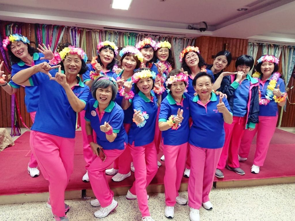 一群身穿蓝色polo衫和粉色裤子、头戴花冠的人在装饰一新的舞台上摆姿势拍照。