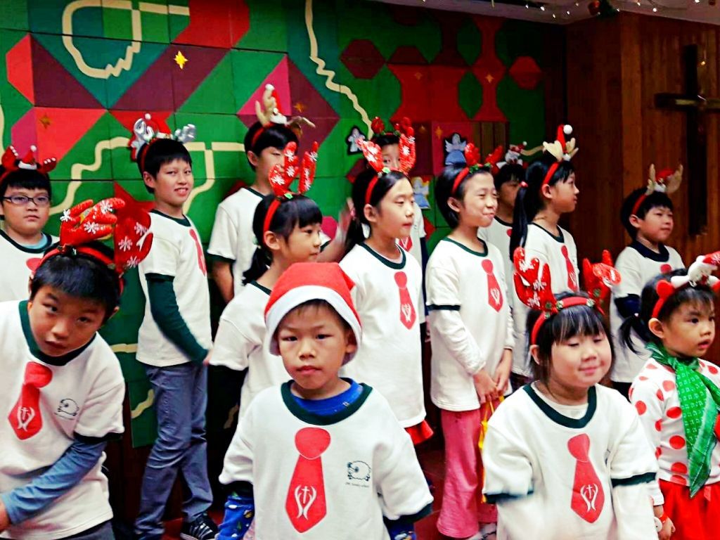 一群戴着驯鹿角、穿着红色领带图案衬衫的孩子站在图案背景前。