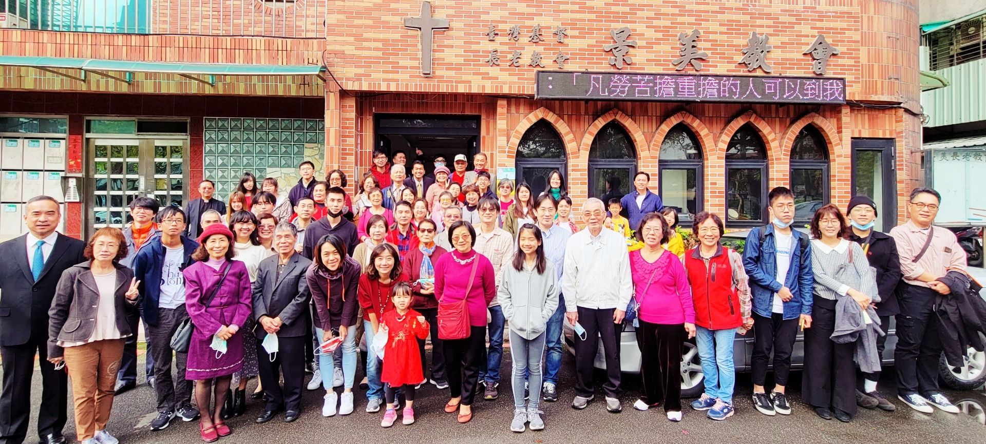 一群人站在一座砖砌教堂外，教堂有拱形窗户，正在摆姿势拍照。