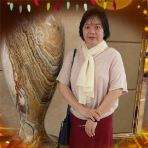 一位留着深色短发、身穿浅色上衣和围巾的人，站在一个大型的、有纹理的装饰花瓶旁边。