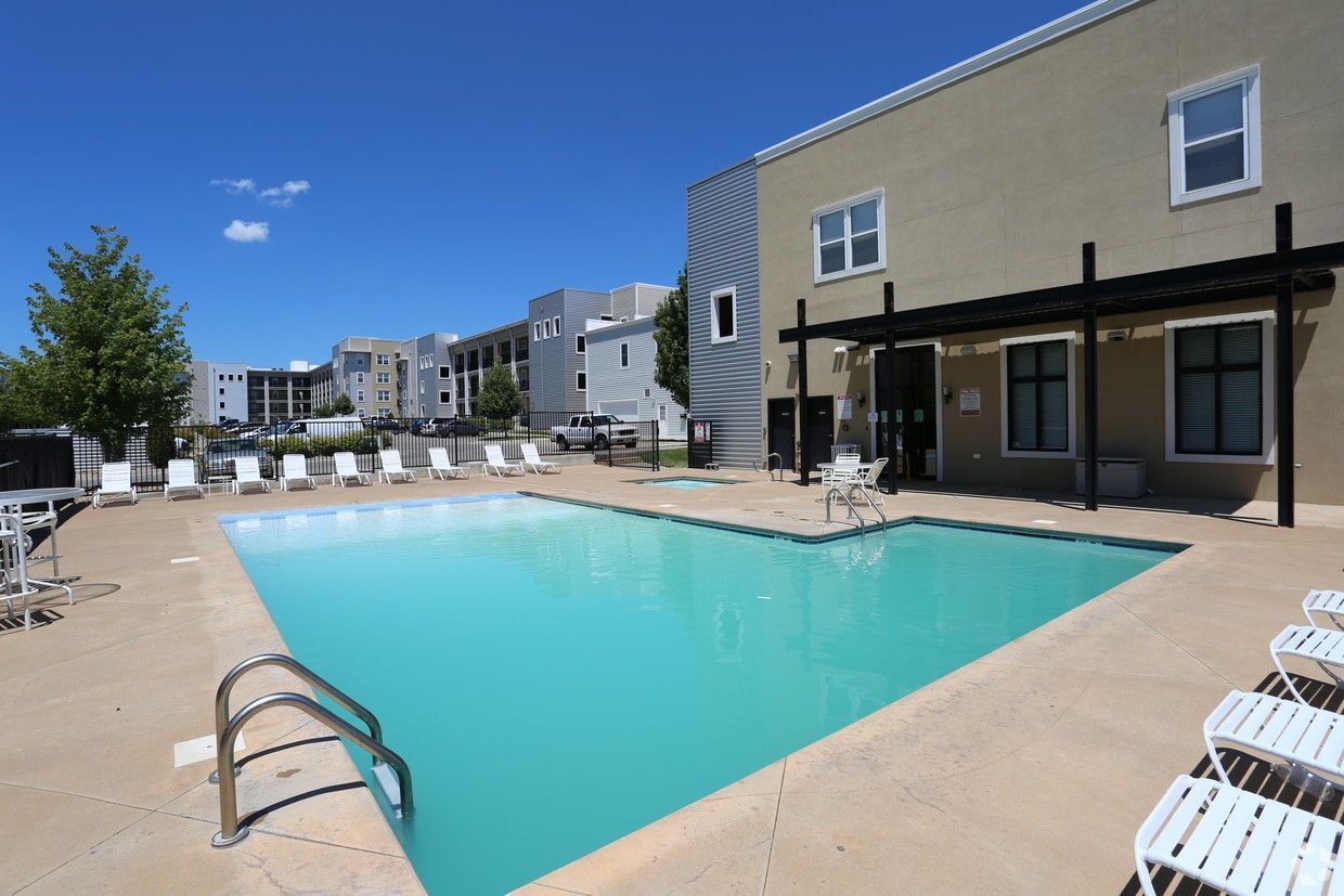 Pool area with lounge chairs, building in the background, blue sky, and turquoise water.