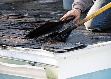 Une personne utilise une pelle pour enlever les bardeaux d'un toit.