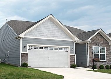 Une maison grise avec une porte de garage blanche et un toit gris.