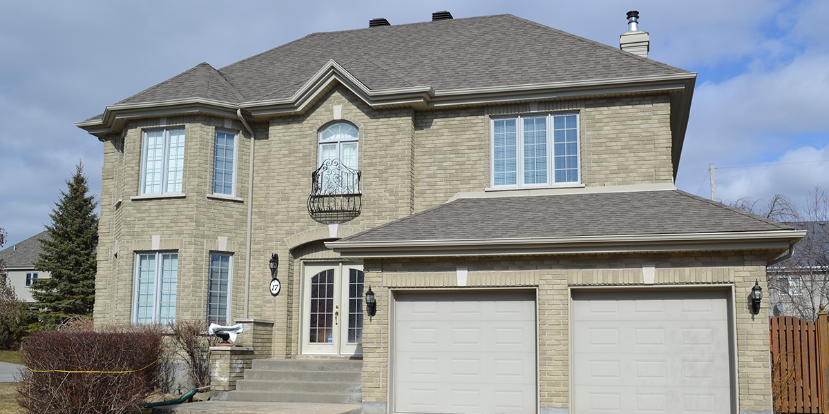 Une grande maison en brique avec deux portes de garage et un toit gris.