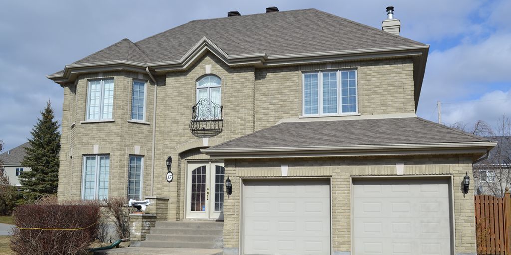 Une grande maison en brique avec deux portes de garage et un balcon