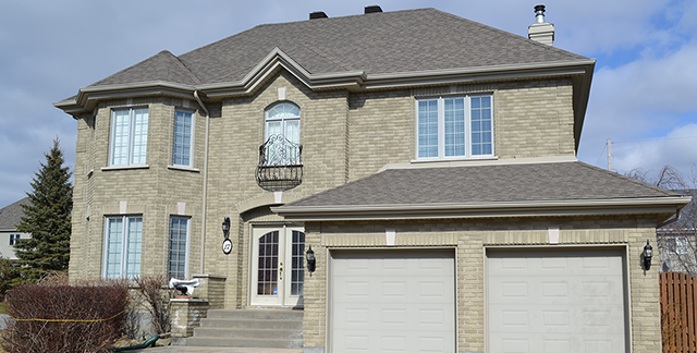 Une grande maison en brique avec deux portes de garage et un balcon.