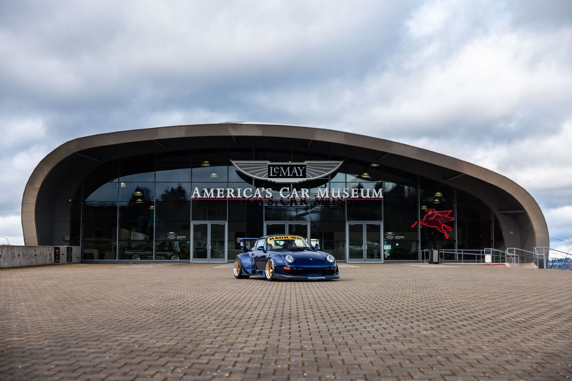 A blue car is parked in front of an american car museum.