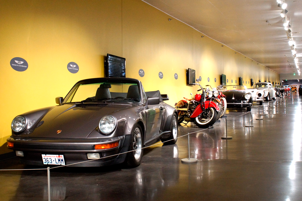 A row of cars and motorcycles are on display in a museum.
