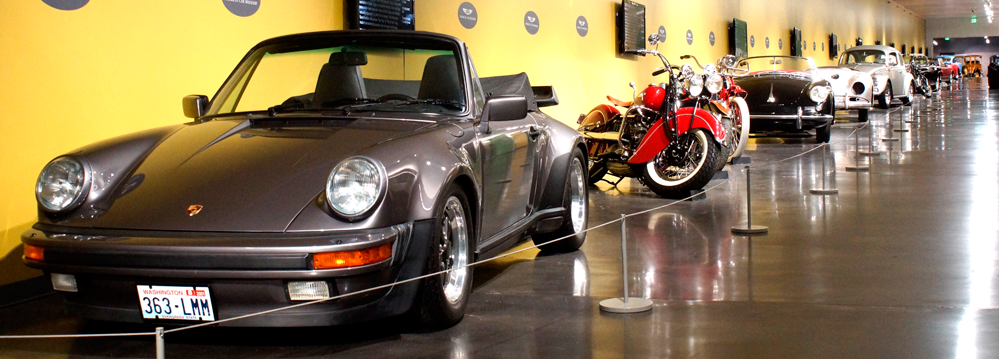 A row of cars and motorcycles are on display in a museum