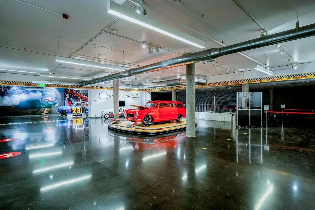 A red car is parked on a circular display in a large room.