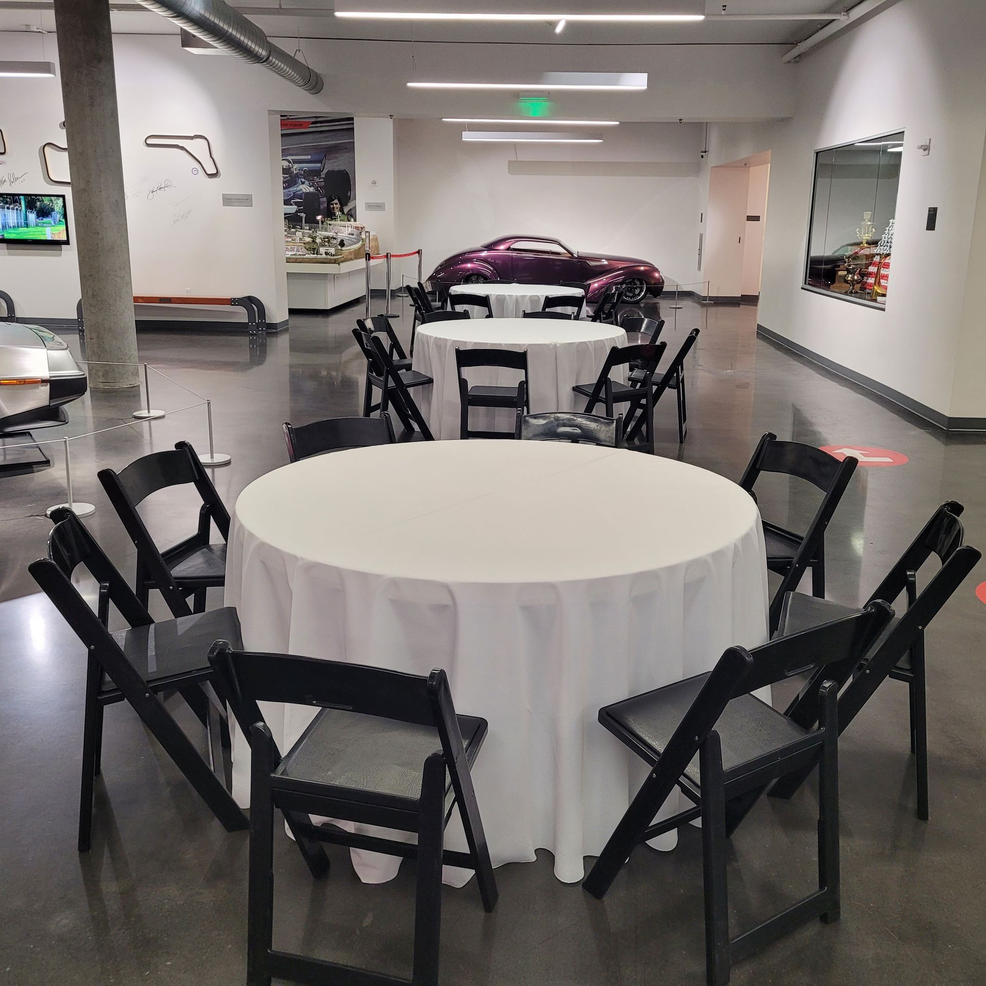 A room with tables and chairs and a purple car in the background