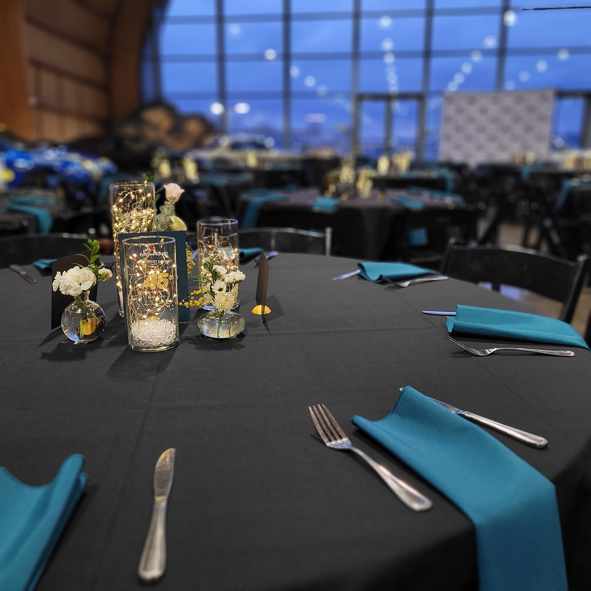A table with a black table cloth and blue napkins
