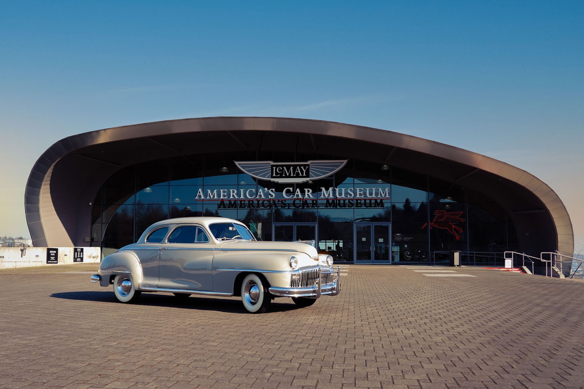 A silver car is parked in front of the american car museum.