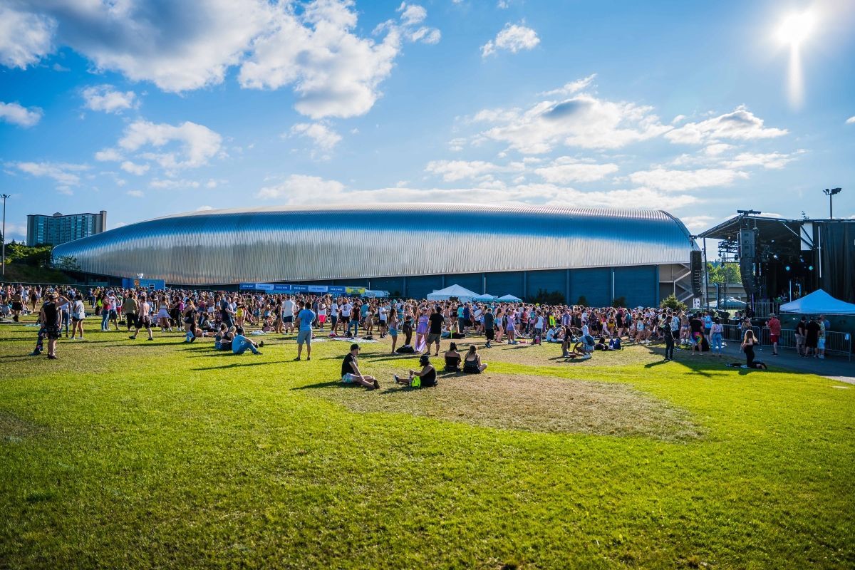 A crowd of people are gathered in a grassy field in front of a large building.