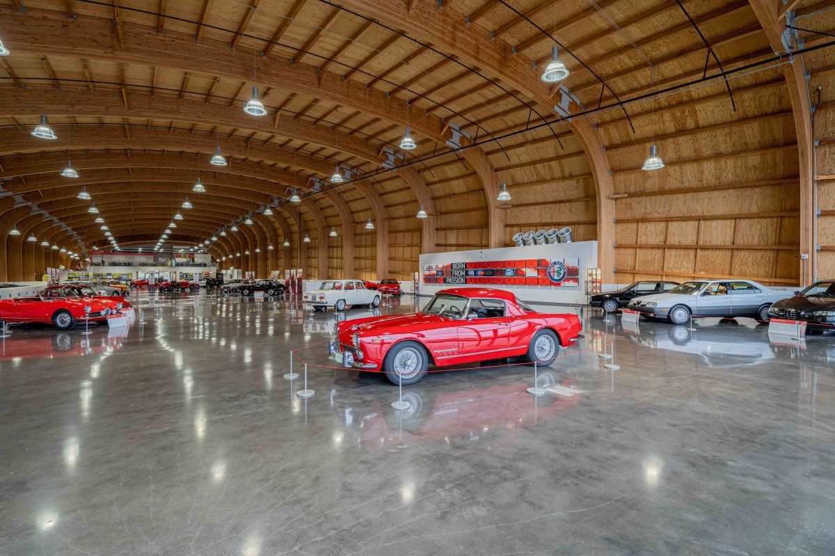 A red car is parked in a large warehouse filled with cars.