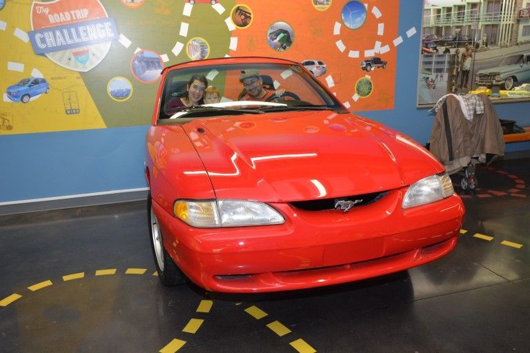 A red car is parked in front of a wall that says road trip challenge