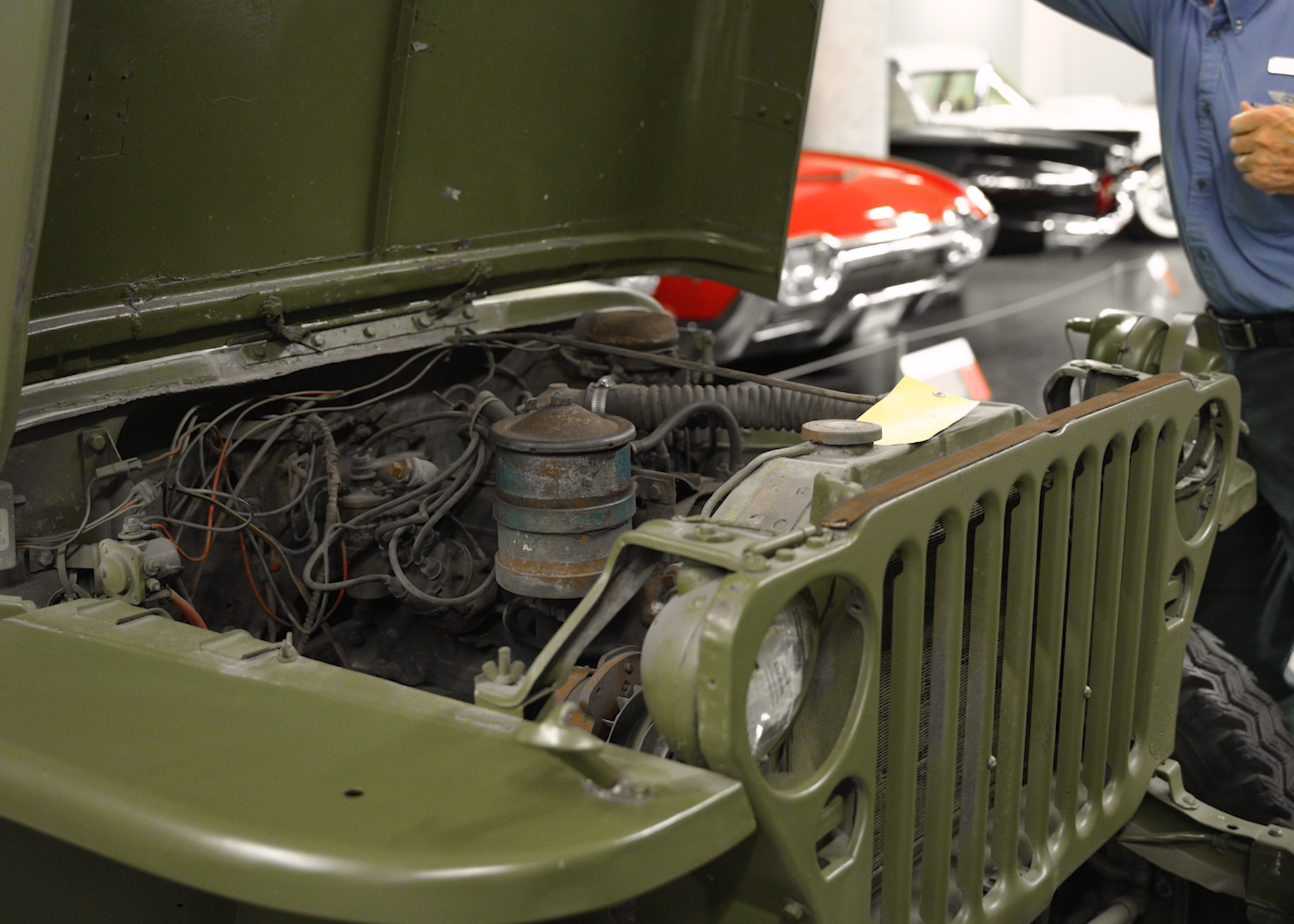 A man is looking under the hood of a green jeep
