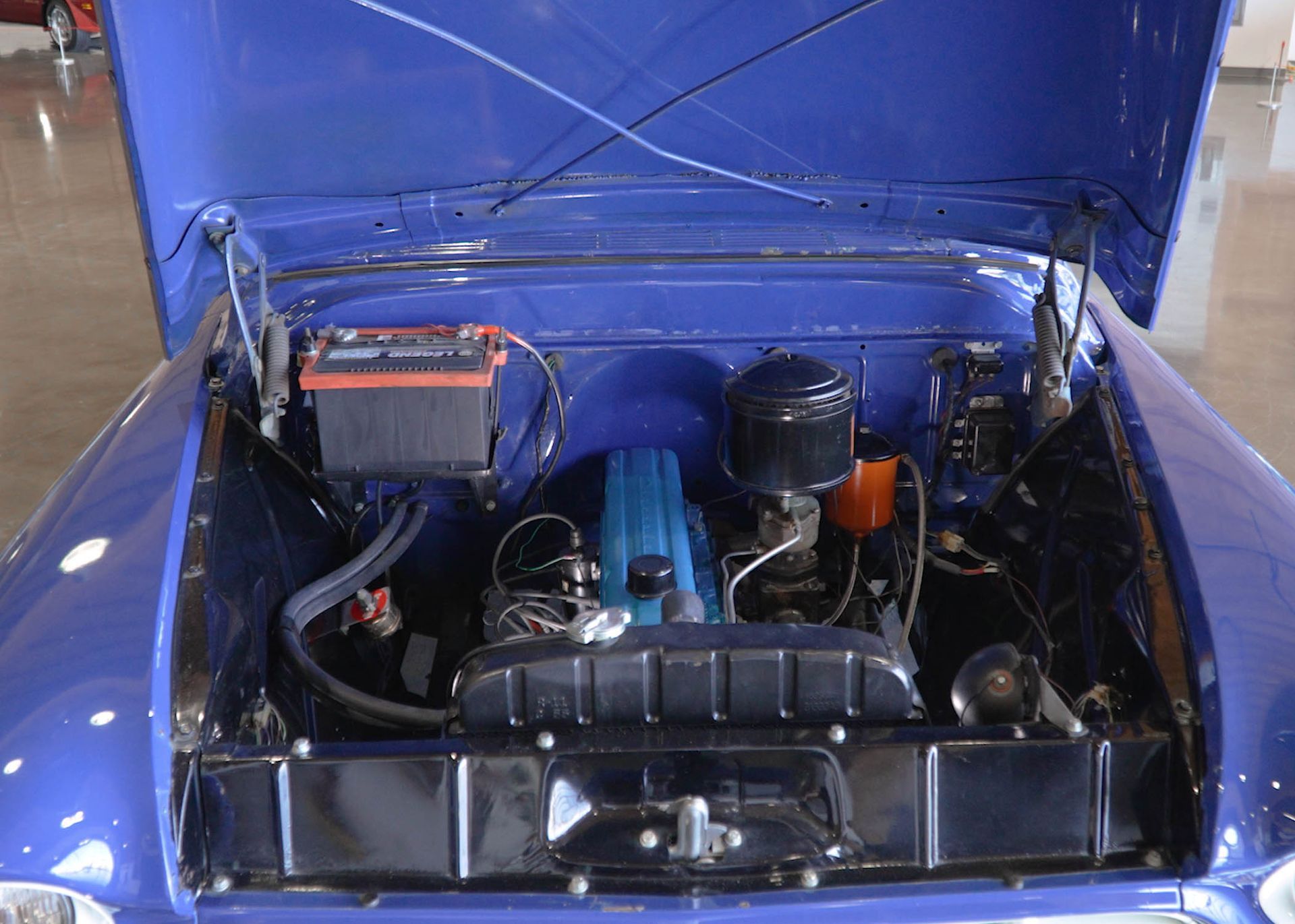 The engine of a blue car is shown with the hood open.