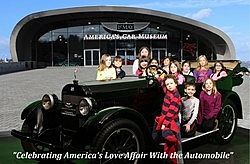 A group of children are posing for a picture in front of an old car.