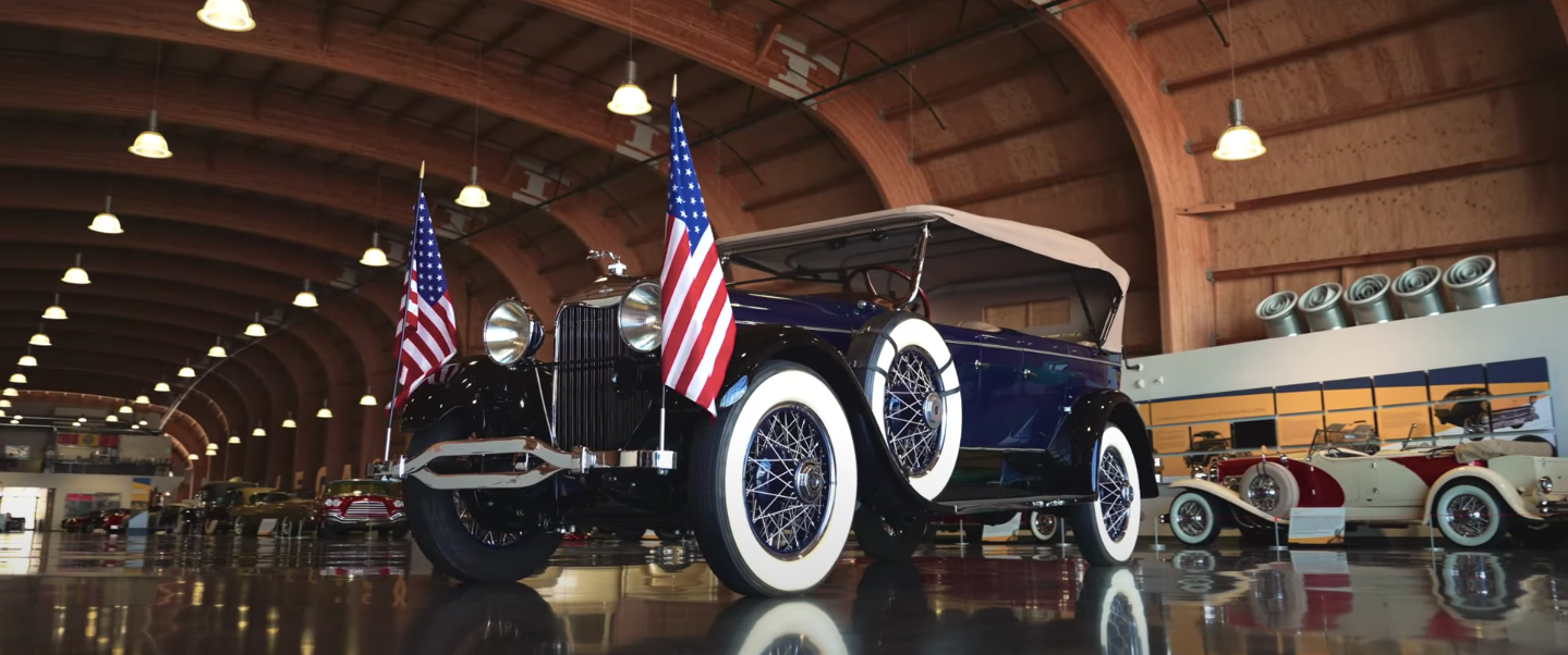 An old car is parked in a garage with american flags on it.