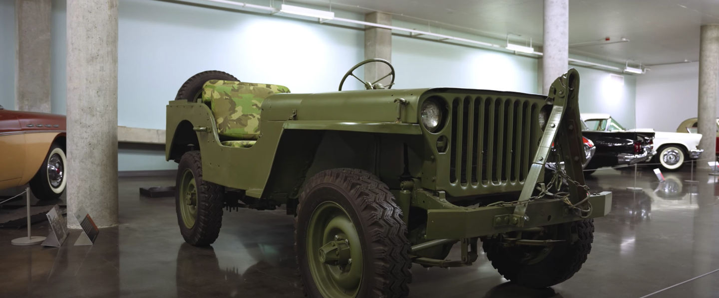 A green jeep is parked in a garage next to other cars.