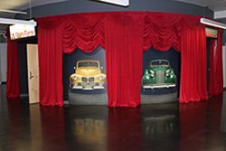 A room with red curtains and a painting of cars on the wall.