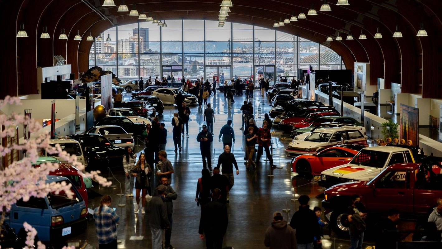 A group of people are walking through a large building filled with cars.