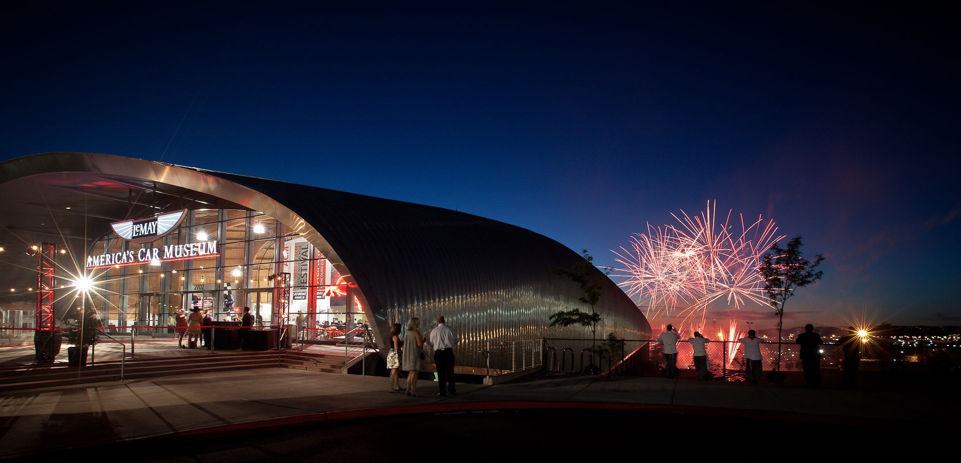 A large building is lit up at night with fireworks in the background.