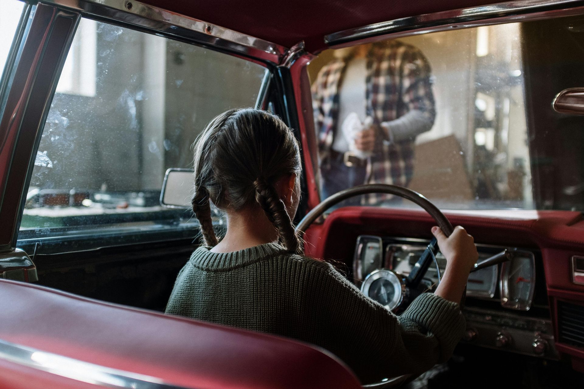 A little girl is sitting in the driver 's seat of a red car.