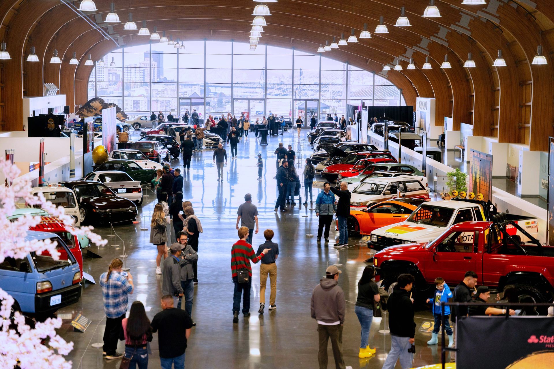 A group of people are standing in a large room with cars on display.