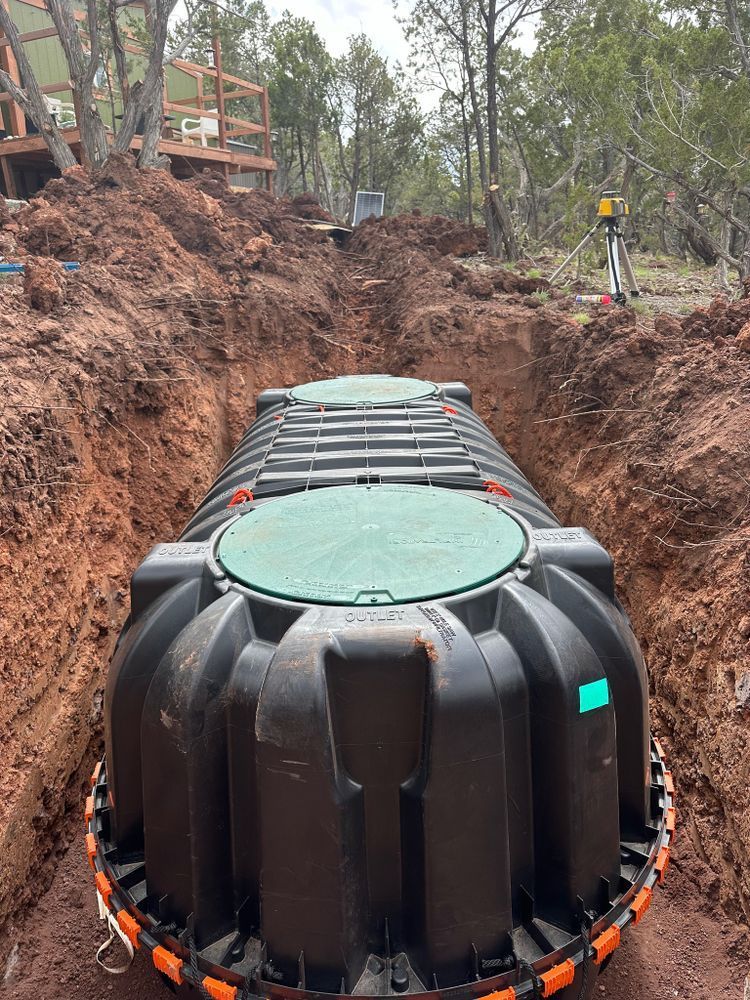 Black septic tank in a trench, ready for burial. Green lids, orange ring, dirt walls.