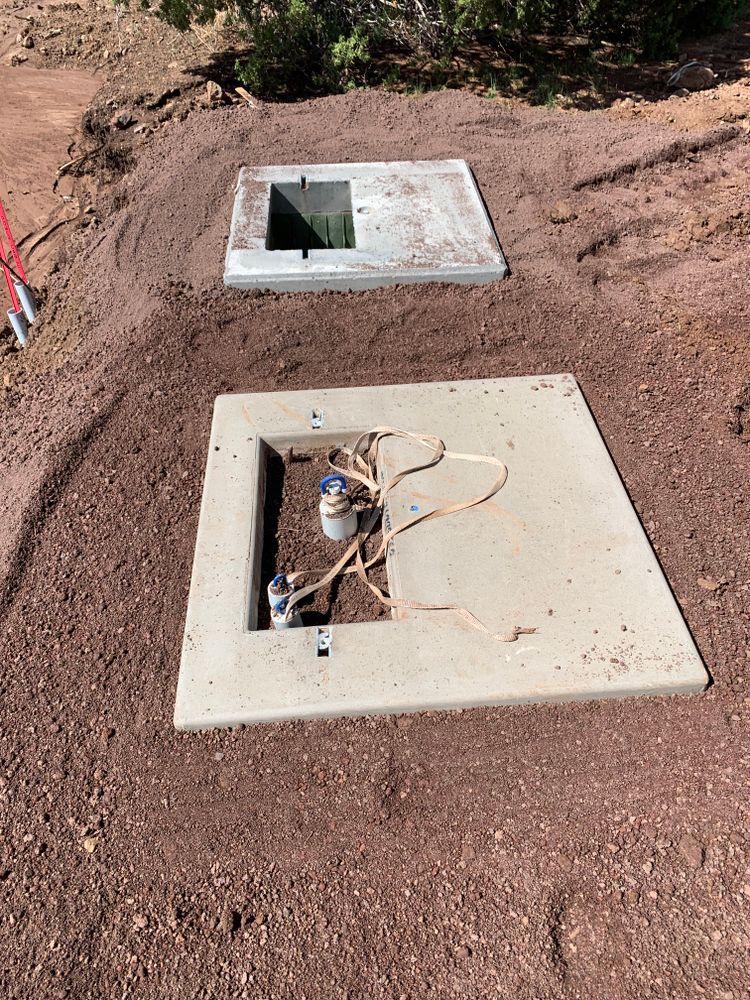 Two open concrete utility boxes in reddish-brown dirt, wires and equipment visible.