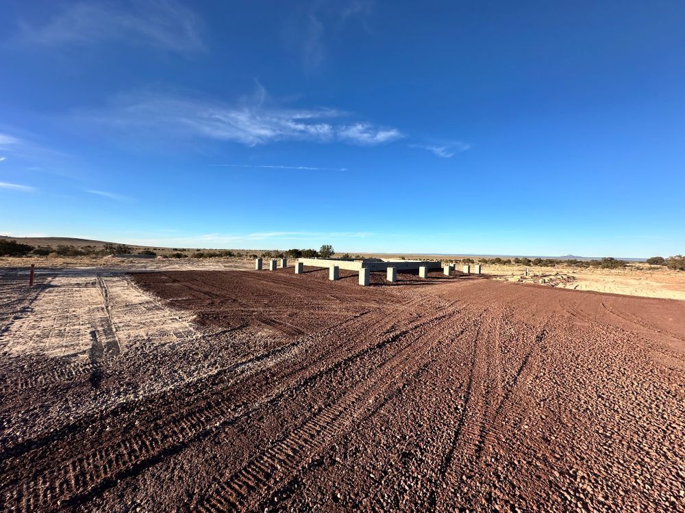 Concrete foundation on red dirt road under a blue sky.