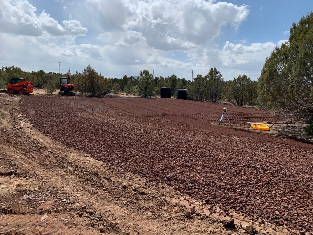 Red rock field being prepared for construction, with two pieces of machinery and a person in the distance.