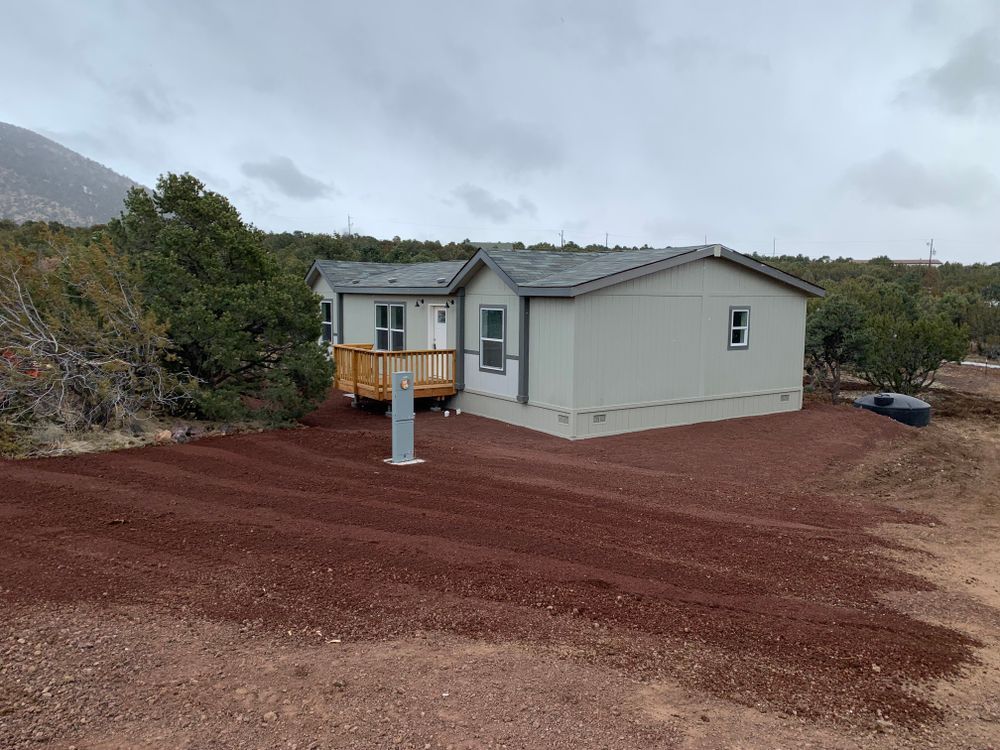 A light grey house on a rocky landscape with a small wooden deck under an overcast sky.