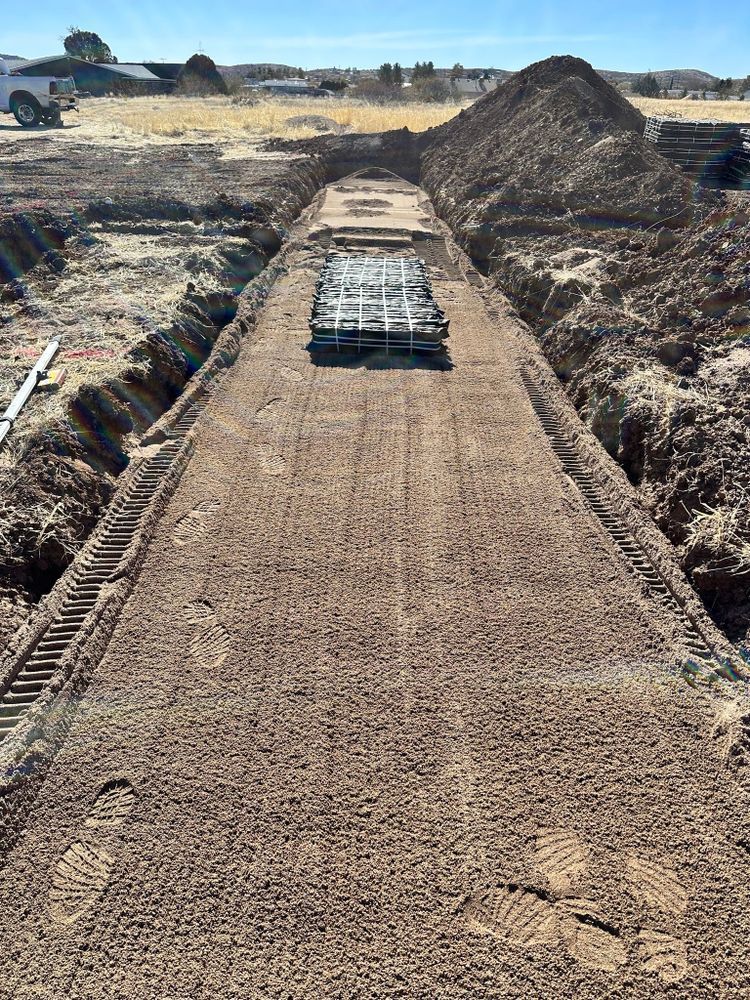 Construction site: trench with gravel base, rebar grid, and piles of dirt on the side.
