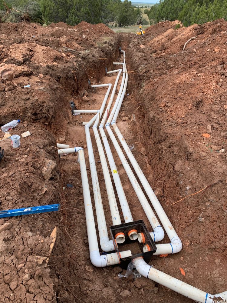 Trench with white PVC pipes being installed for underground utilities on a construction site.