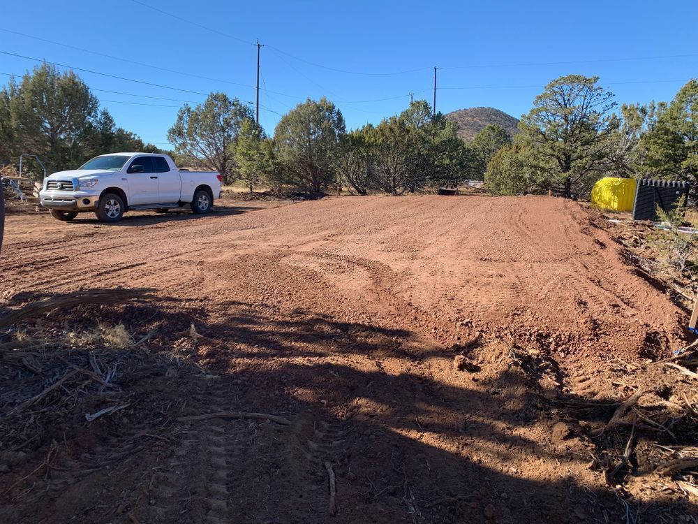 A cleared plot of red dirt with a white pickup truck, ready for construction under a blue sky.