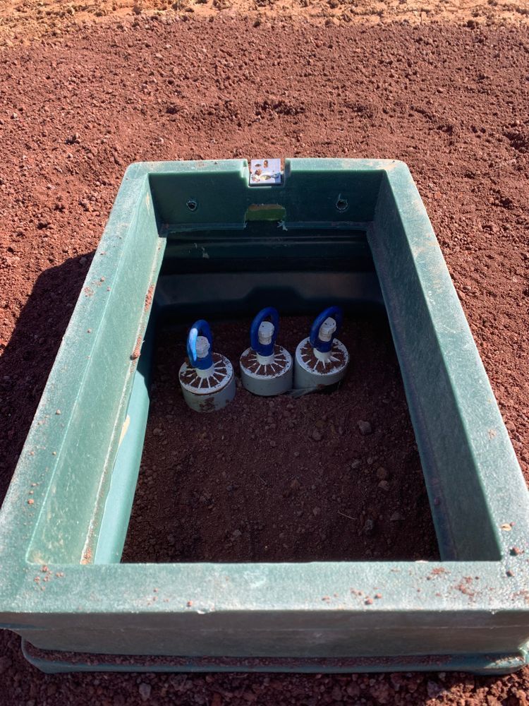 Green utility box in dirt, containing three blue and white valve caps.