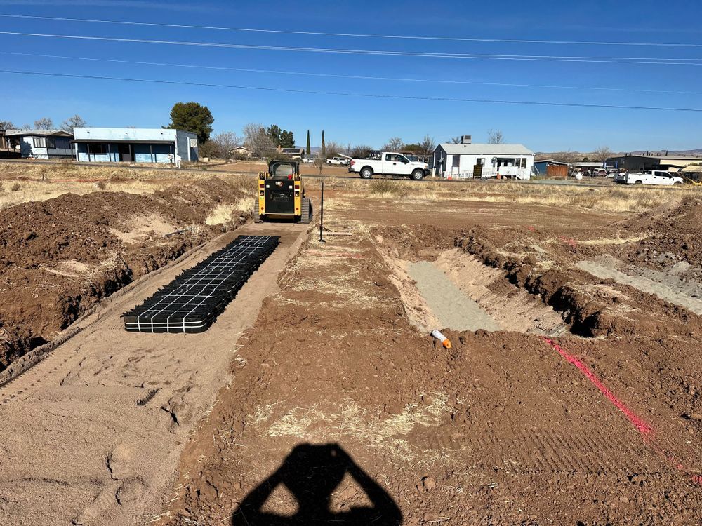 Construction site with trenches, small tractor, and modular drainage system. Houses in the background.