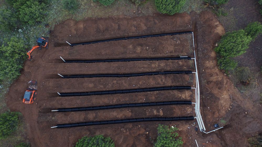 Aerial view of construction site with rows of black material in dug trenches and small excavators.