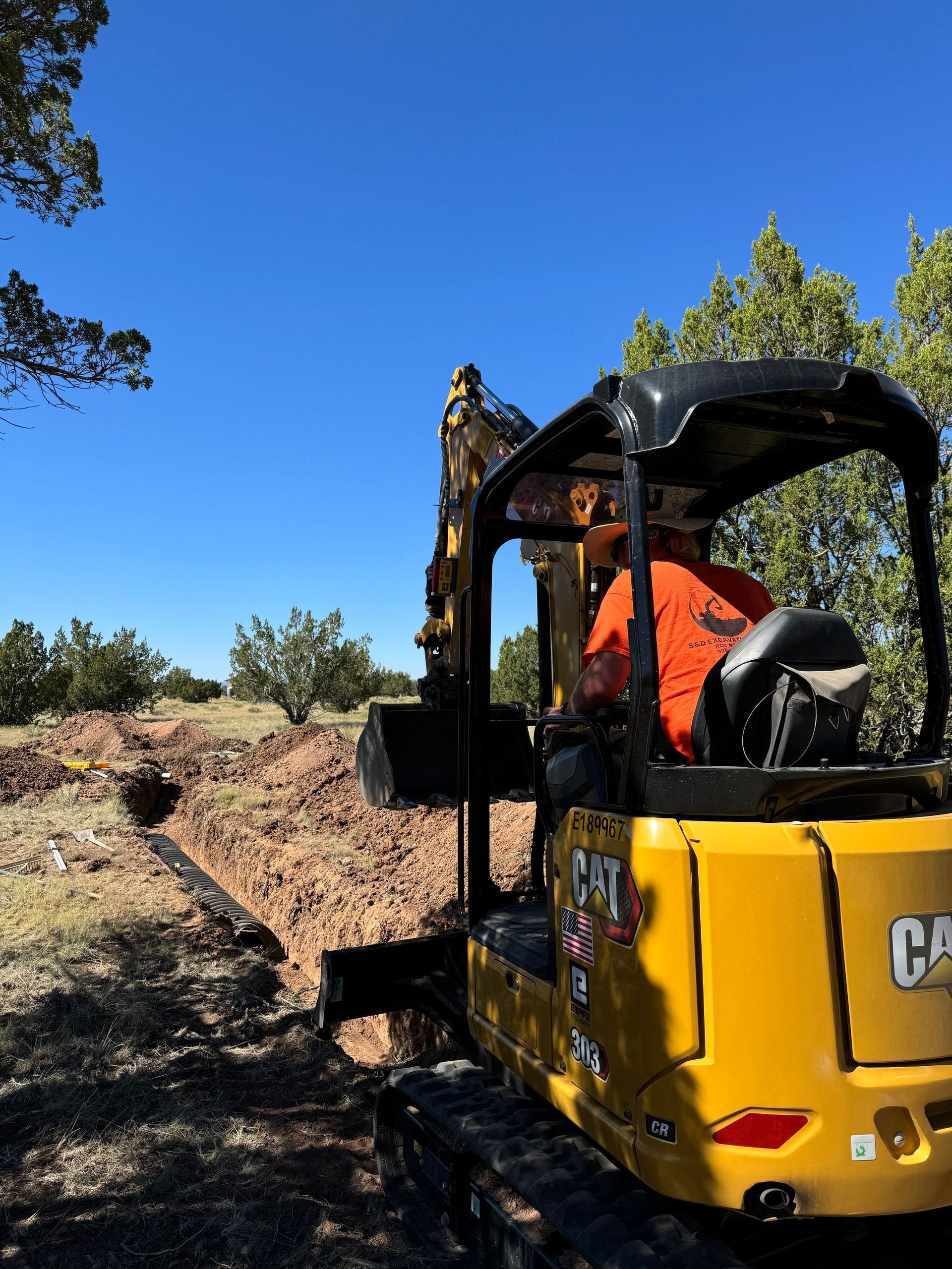 A yellow excavator digging a trench in the dirt under a clear blue sky.